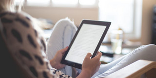 Frau liest E-Book Eine Frau sitzt in einem Sessel und liest ein E-Book