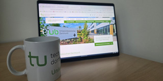 Bildschirm mit Tasse Eine Tasse mit TU-Logo steht vor einem Bildschirm.