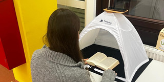 Scanzelt für Smartphone Junge Frau scannt mit ihrem Smartphone Seiten aus einem Buch ein, das unter einem Scanzelt liegt.