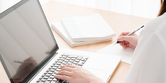 Junge Frau am Laptop Junge Frau im Profil sitzt an offenem Laptop an einem Tisch, daneben Bücher