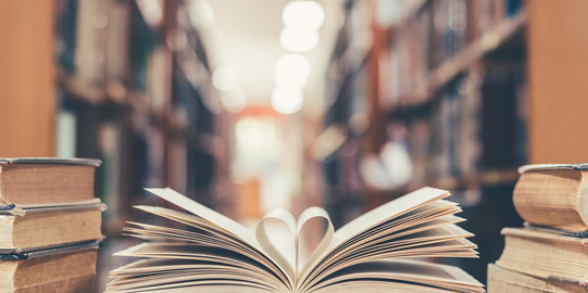 Aufgeklapptes Buch mit herzförmigen Seiten in der Mitte Ein aufgeklapptes Buch liegt mit zu einem Herz geformten Seiten auf dem Tisch neben weiteren Büchern