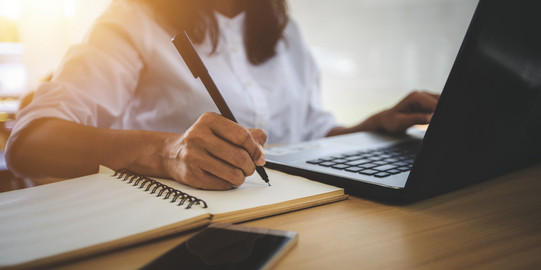 Junge Frau lernt am Laptop Eine junge Frau lernt am Laptop und schreibt in ein Heft