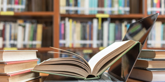 Aufgeklapptes Buch in Laptop Aufgeklapptes Buch liegt in aufgeklapptem Laptop vor und neben weiteren Büchern