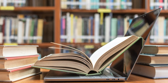 Aufgeklapptes Buch in Laptop Aufgeklapptes Buch liegt in aufgeklapptem Laptop vor und neben weiteren Büchern