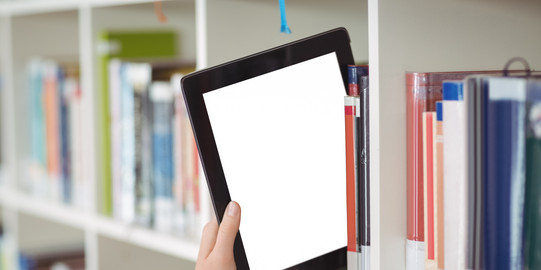 Hand zieht Tablet aus einem Bücherregal Eine Hand zieht ein Tablet aus einem Bücherregal in einer Bibliothek