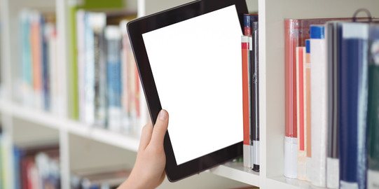 Hand zieht Tablet aus einem Bücherregal Eine Hand zieht ein Tablet aus einem Bücherregal in einer Bibliothek