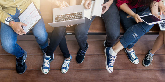 Junge Menschen lernen mit Tablet und Laptop Die Beine von fünf jungen Menschen, die mit Tablet und Laptop lernen