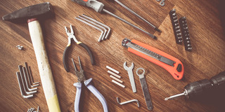 Werkzeuge auf Holztisch Auf einem Holztisch liegen ein Hammer, verschiedene Zangen, Imbusschlüssel, Schrauben, Schraubenzieher, Dübel etc.