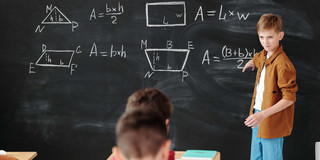 Junge an Tafel Ein Junge steht an der Tafel und erklärt Mathe