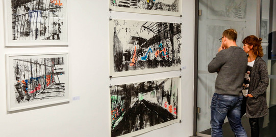 Ausstellung Zwei Menschen betrachten Bilder an der Wand in einer Ausstellung.